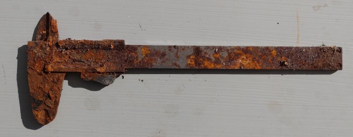Rostigt gammalt verktyg, troligen en hammare, ligger mot en vit bakgrund.
