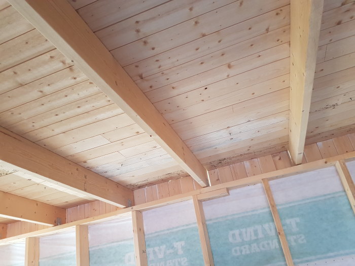 Träkonstruktion av ett tak med isoleringsskiva, ej färdigställt, synliga takbjälkar och isoleringsmaterial.
