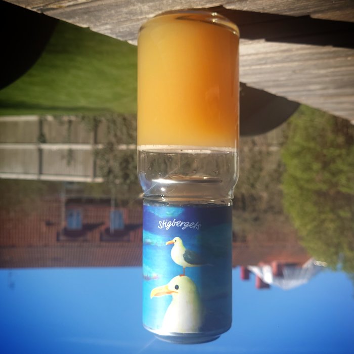 Ett omvänt glas med orange dryck på spegelblank yta, himmel reflekterad, märkt "tigfärgeek."