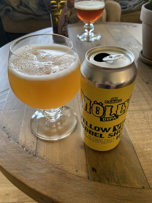 Ölglas med skum på träbord bredvid öppen burk, annat glas i bakgrunden.