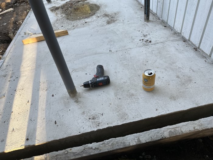 Byggarbetsplats med betonggrund, skruvdragare, ölburk. Oavslutade arbeten, verktyg och avslappningssymboler.