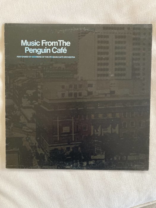 Albumomslag: "Music From The Penguin Café", urbant landskap, mörk ton, text upptill, skugglika byggnader.