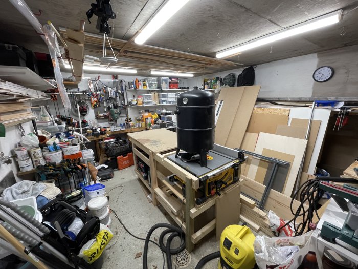 Välutrustad verkstad med verktyg, maskiner och material. Oorganiserad, trångt, DIY-projekt. Klocka på väggen.