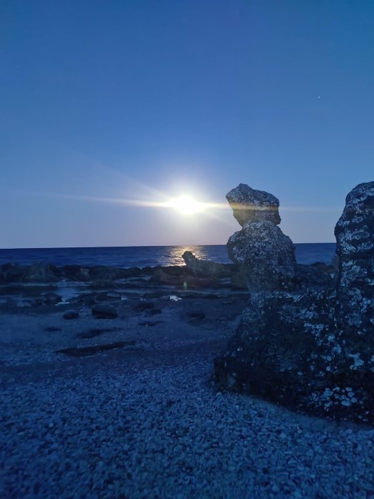 Klippformation vid havet, solnedgång eller soluppgång, stenstruktur i förgrunden, lugnt vatten, klar himmel, en stjärna synlig.