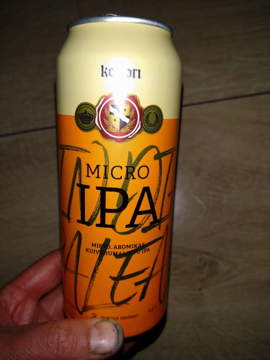 Burk med öl märkt "MICRO IPA", hålls i hand. Etikett text på finska, bryggerilogotyp. Orange/vit färgsättning.