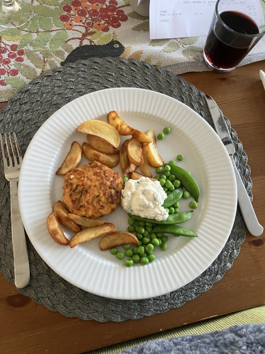 En tallrik med mat: kroketter, gröna ärter, sockerärtor, vit sås, glas röd dryck.