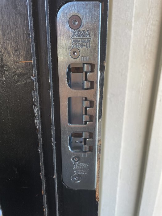 ASSA låsbeslag på dörrkarm, slitage, säkerhetsutrustning, metall mot trä, skruvfästen synliga.