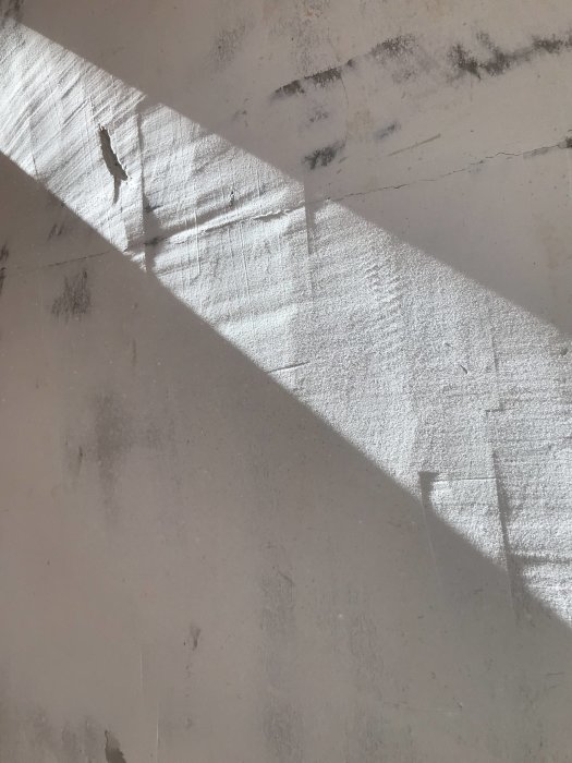 Ljusstrålar som faller på en ojämn vit vägg, skuggor, textur, spricka synlig, suggestiv stillhet.