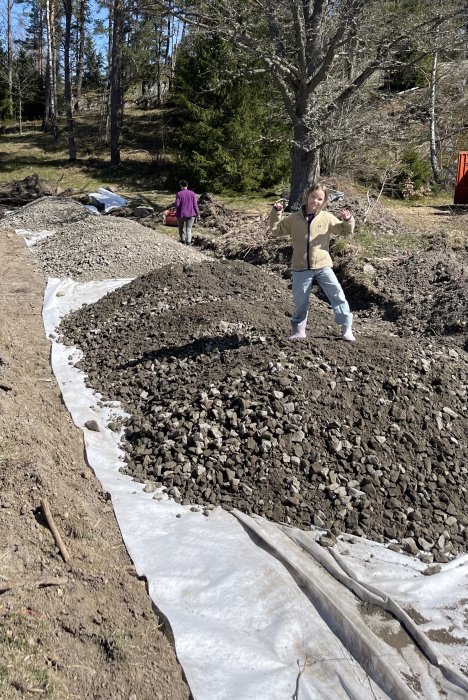 Utomhus, barn leker på grushög, en annan person i bakgrunden, naturlig miljö, soligt, dagtid.