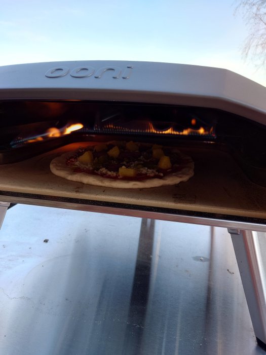 Pizza i en bärbar ugn med märket "Ooni", utomhus på dagen.