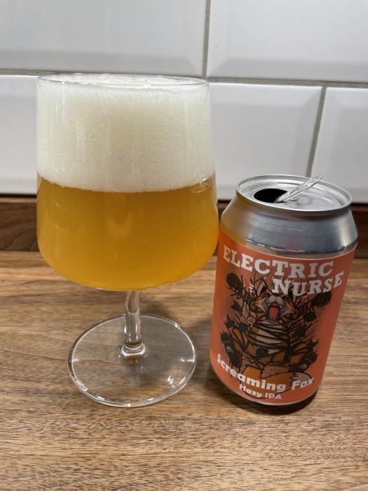 Ett glas med skummande öl bredvid en öppnad burk, märkt "Electric Nurse Screaming Fox Hazy IPA".