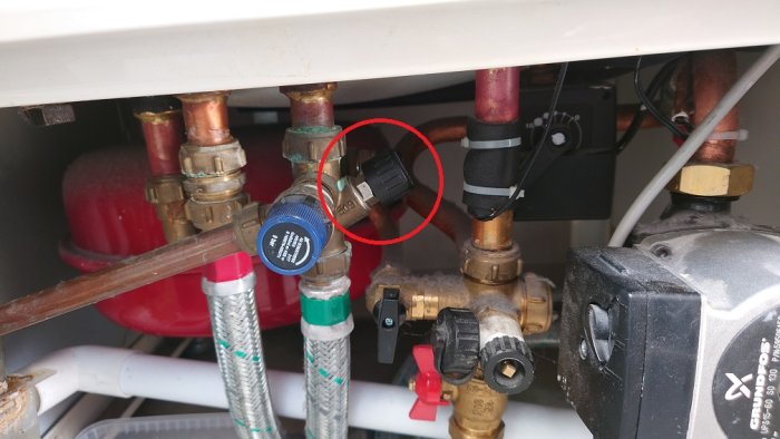 VVS-installation med rör, ventiler och mätare under diskbänk, potentiellt läckage markerat med röd cirkel.