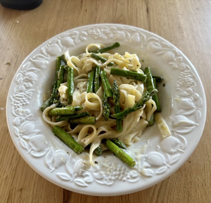 En tallrik med pasta och sparris på ett träbord.