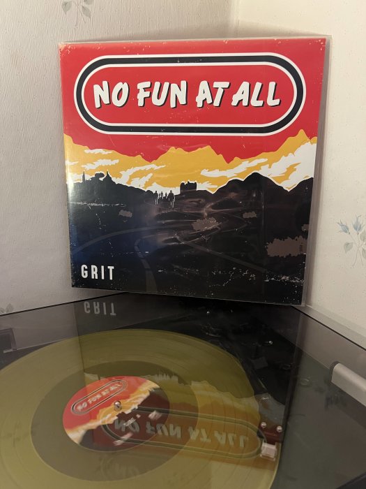 Skivomslag "NO FUN AT ALL - GRIT", genomskinligt gul vinylskiva på en skivspelare.