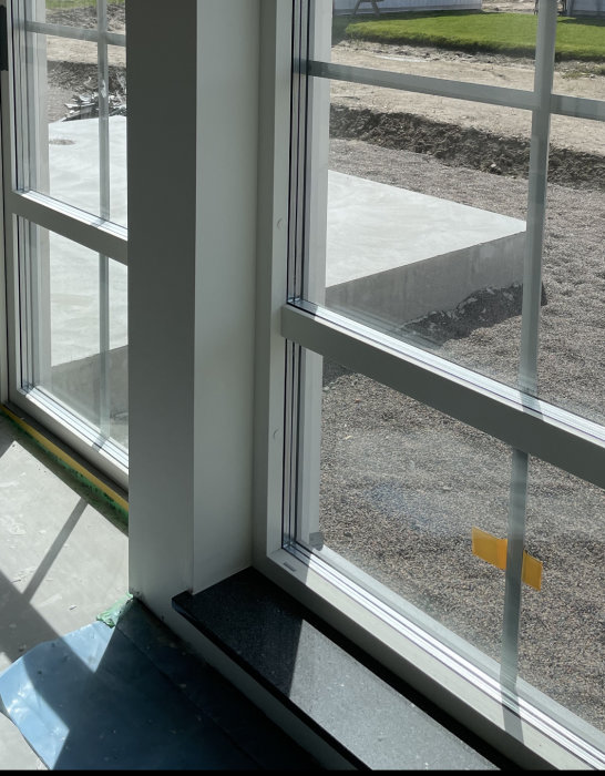 Solljus genom fönster i ett tomt rum med utsikt över en byggarbetsplats utomhus.