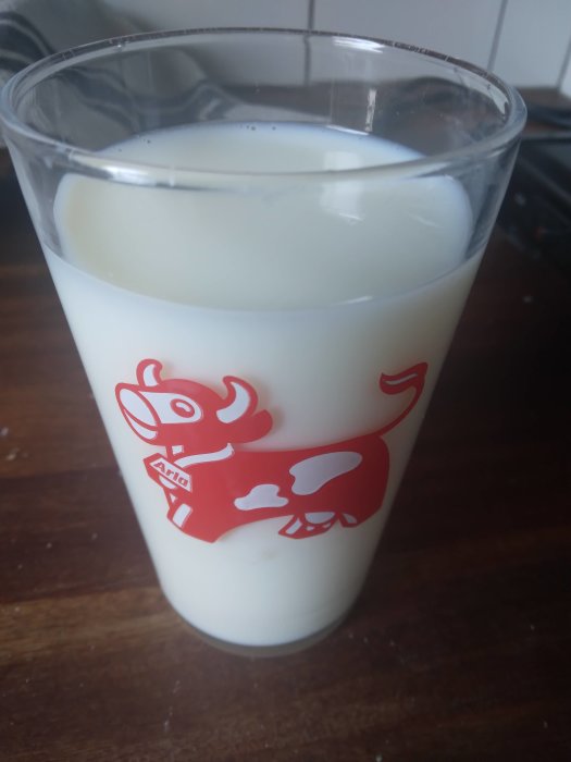 Ett glas mjölk med röd tecknad ko på sidan, står på träyta.