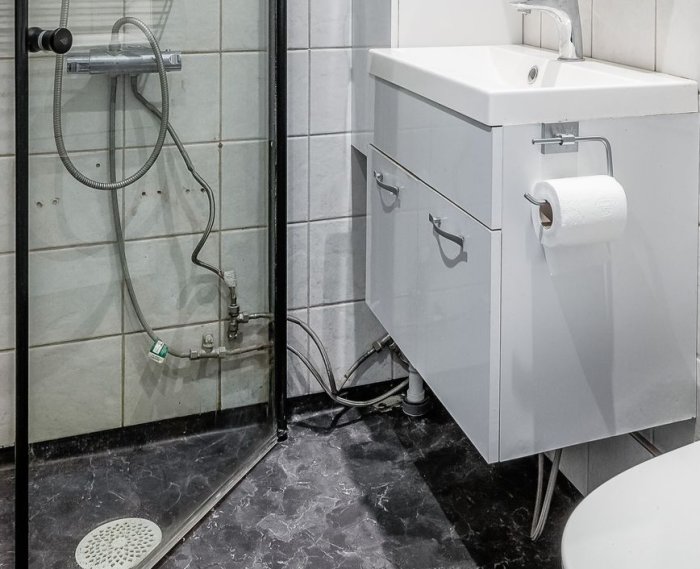 Ett modernt badrum med duschhörn, handfat och toalettpapper i vit och grå färgsättning.