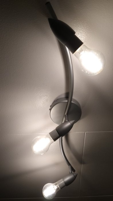 Vägglampa med tre tända ljuskällor och böjda armar på en ljus vägg.