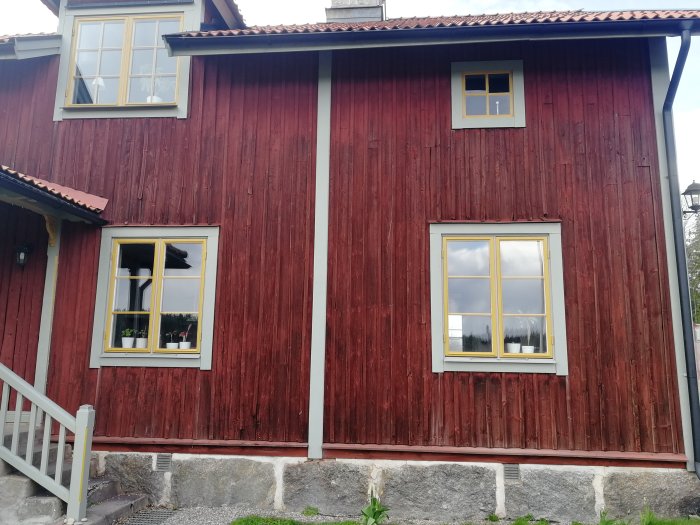 Röd träfasad, vita fönster, grund av sten, traditionellt hus, svenska färger, grå himmel, trappa.