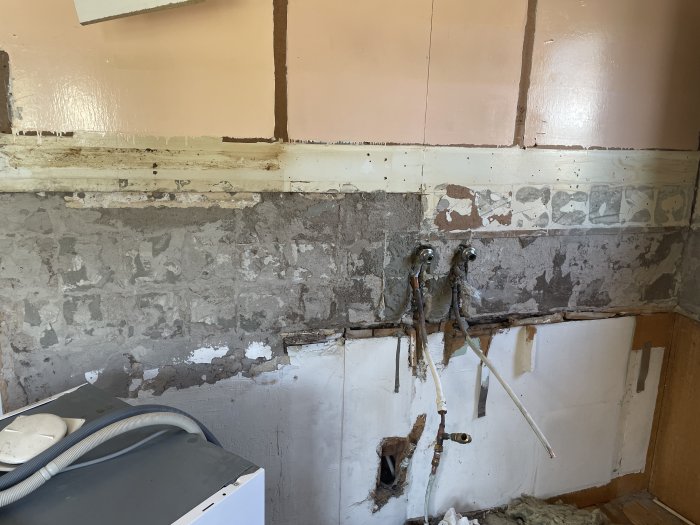 Renovering; avskalade väggar, exponerade rör, gammal vitvaru, öppningar i väggen, spackel, renoveringsarbete pågår.