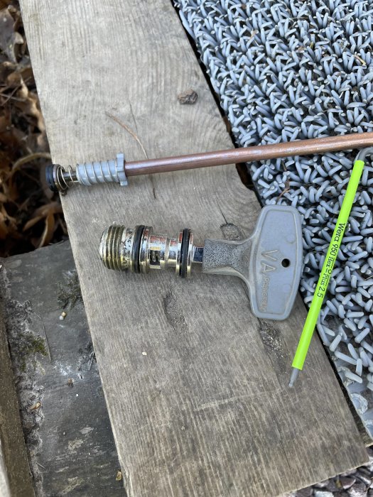 En slangkoppling och en grön penna på träbräda bredvid gråa småstenar.