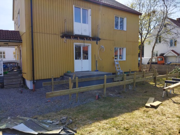 Gult hus, byggprojekt pågår, stegar, oavslutad träkonstruktion, byggmaterial, utomhus, dagtid.