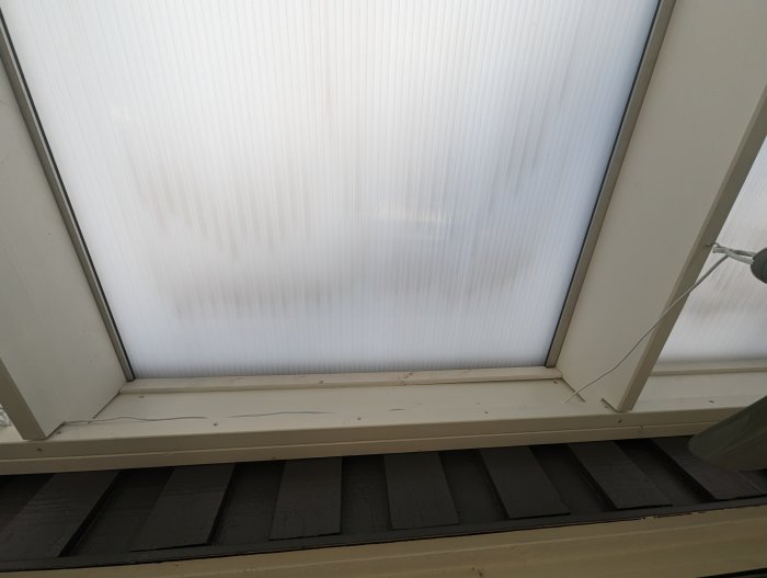 Fönstertak av mattglas med synligt träbjälklag och del av takfönstrets vitmålade ram.