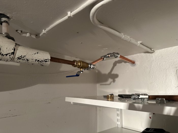 Vattenrör med ventil under tak, skuggspel, ommålad isolering, hyllkonsoler, vit vägg.