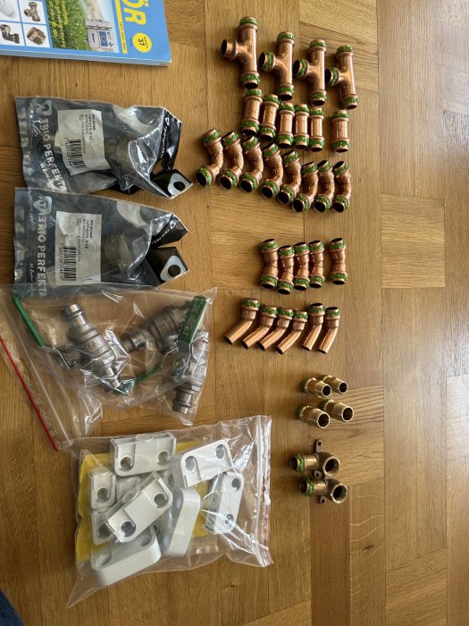 VVS-material på trägolv: kopplingar, rör - olika storlekar och former, förpackade fästelement, bakgrund med installationsbok.