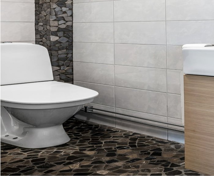 Modernt badrum, vitt toalettstol, grå kakelvägg, mörka stengolvstenar, dekorativ stenpelare.