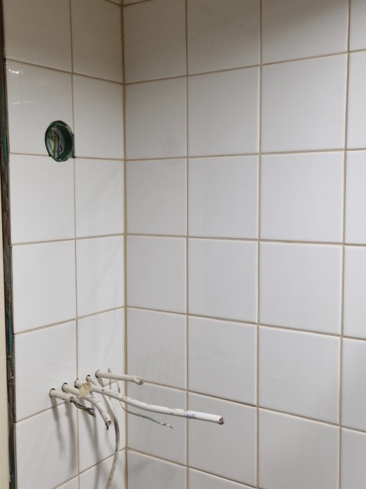 Kaklad vägg med oskyddade elektriska kablar och öppen eldosa. Renoveringsbehov i badrum.