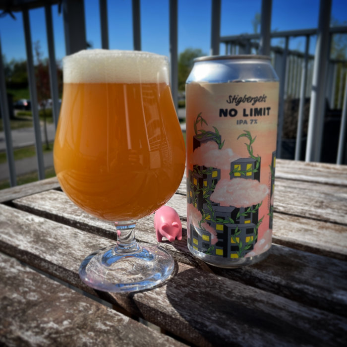 Ölglas med skum, burk "No Limit IPA", träbord, solig dag, rosa grisfigur, utedäck.