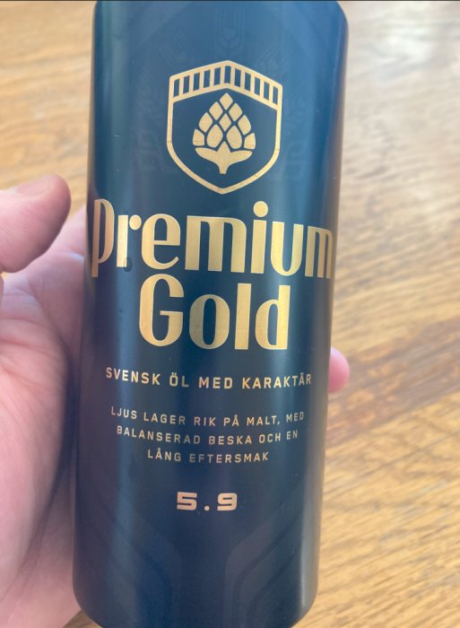 Ölburk med text "Premium Gold, Svensk öl med karaktär", guldteckst, mörk bakgrund, alkoholhalt 5.9%.