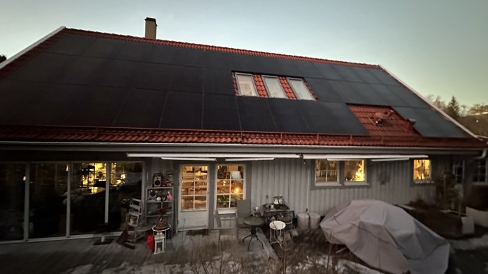 Ett hus med solpaneler på taket, kvällsbelysning, täckt möbel, trädgårdsdekor, och snörester.