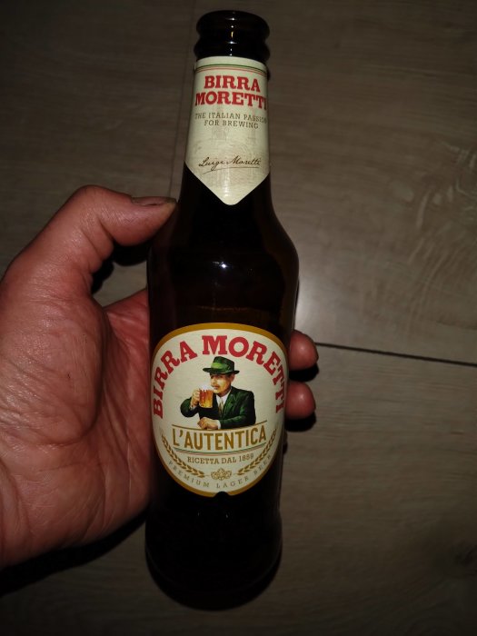 Hand håller Birra Moretti-flaska, italienskt ölmärke, logotyp, premium lager, etikett med man som dricker.