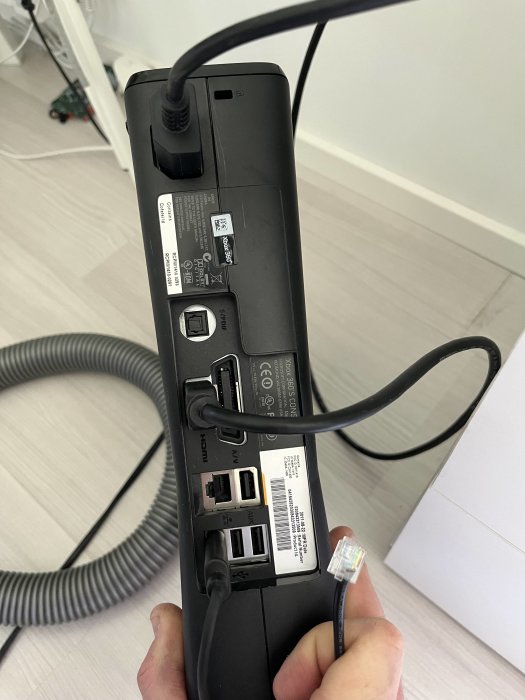 Telefon håller en svart dockningsstation med kablar och portar för anslutningar såsom USB och HDMI.