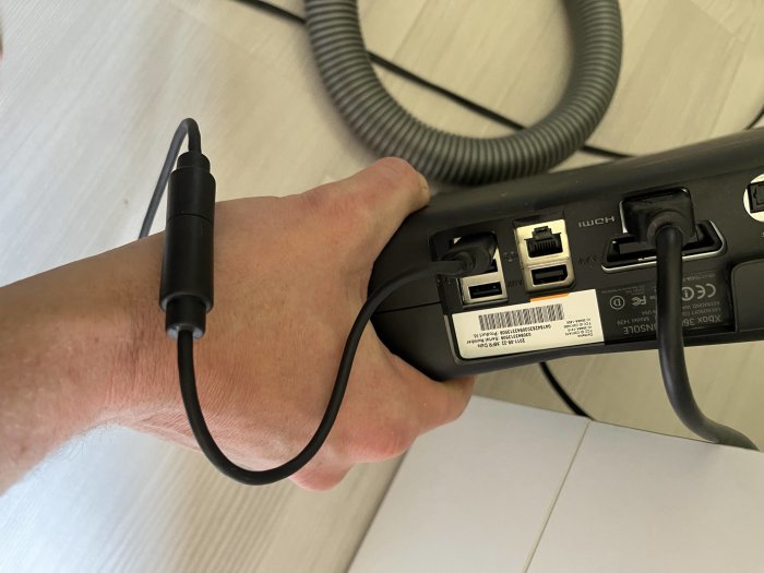 En hand håller en bärbar datorladdare med anslutna kablar nära ett uttag.