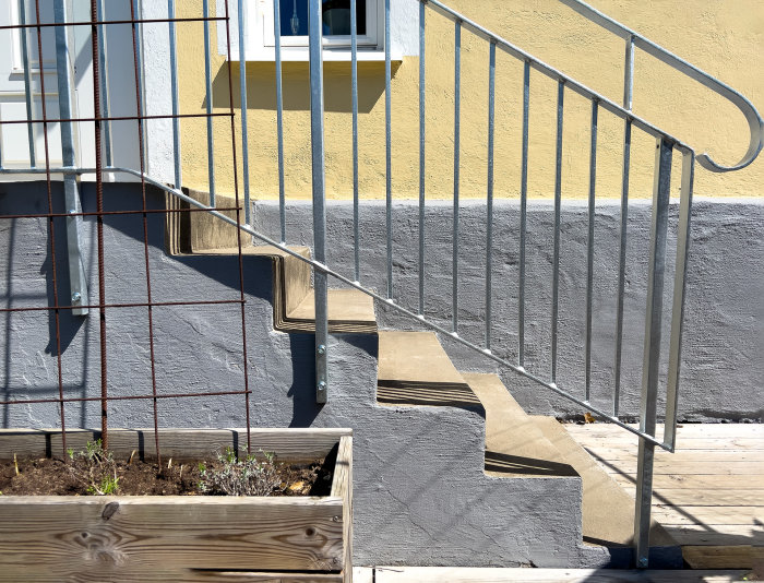 Solbelyst trappa, rekkverk, planteringslåda, skuggspel, grå och gul fasad, dagtid.