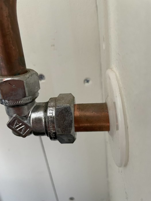 Röranslutning med en ventil, kopparledning, vit vägg och droppande vatten.