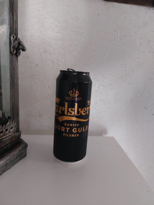 Ölburk av märket Carlsberg, "Sort Guld", står på vit yta bredvid träram.