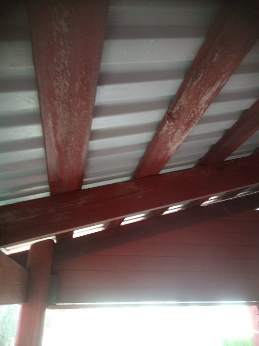 Undertak av metall med röda träbjälkar, något sliten färg, otydligt fokus, inomhus- eller utomhuskonstruktion.