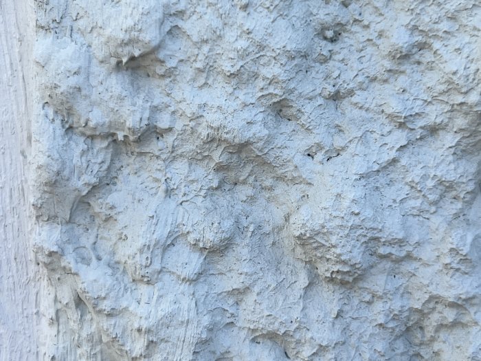 Texturerad, ljusgrå yta, möjligtvis en betongvägg, sliten med oregelbunda mönster och små håligheter.