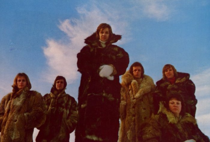 Grupp personer i pälskappor mot blå himmel. Kallt, vintagekänsla, troligen historiskt foto.