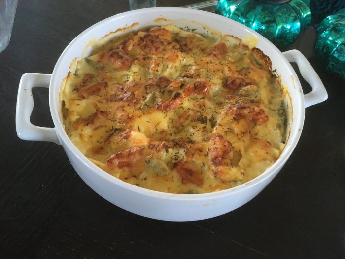 En ugnsbakad gratäng med gyllenbrun ost, örter och grönsaker, serverad i en vit keramikform.
