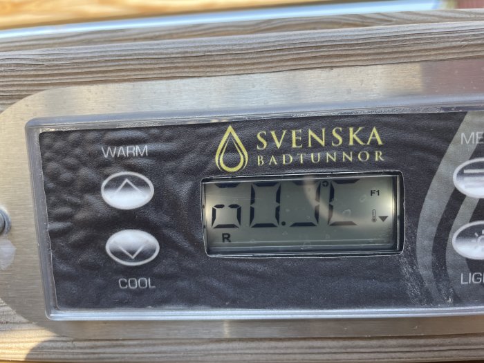 Kontrollpanel för badtunna med temperaturvisning på 38,9°C och knappar för justering av värme. Etikett "SVENSKA BADTUNNOR".