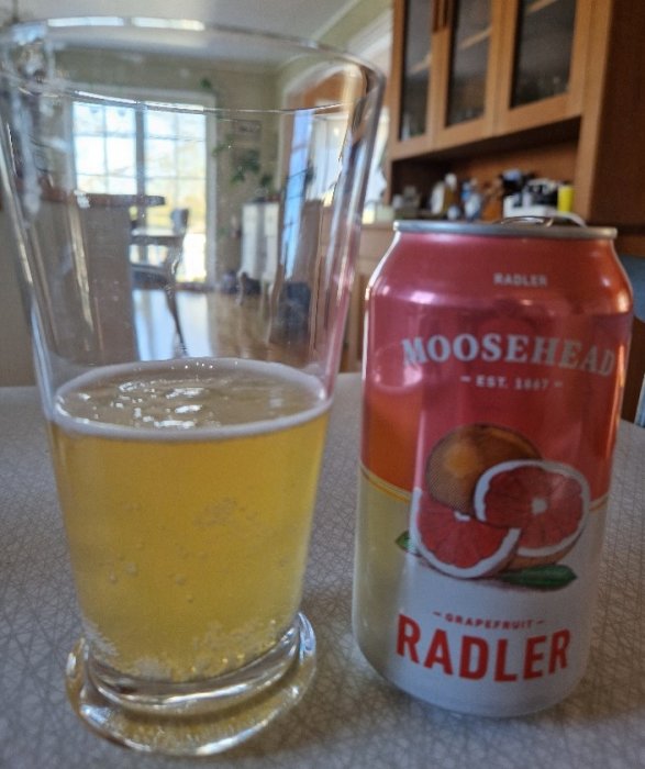 Ett glas med öl och en burk Moosehead Radler på ett bord inomhus.