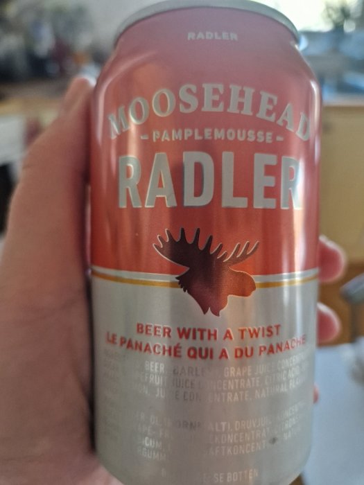 En hand håller en ölburk, Moosehead Radler, med grapefruktsmak mot en otydlig bakgrund.