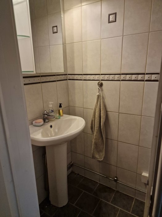 Ett litet badrum med handfat, spegel, tegelvägg och handduk.