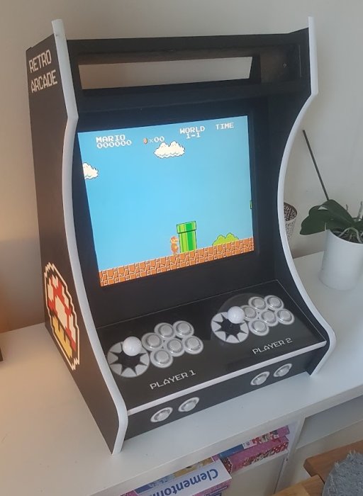 Bärbar arkadmaskin med klassiskt spel, två spelarkontroller, "Retro Arcade"-branding, på en vit yta.