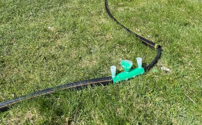 Grön gräsmatta med svart slang och grön sprinkler. Bevattningssystem för trädgård. Soligt väder.